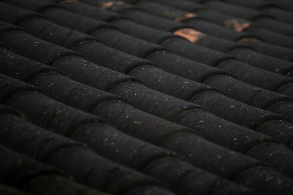 Close view of curled and cracked asphalt shingles on a sloped residential roof with scattered granules in the gutter.