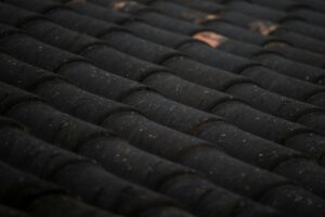 Close view of curled and cracked asphalt shingles on a sloped residential roof with scattered granules in the gutter.